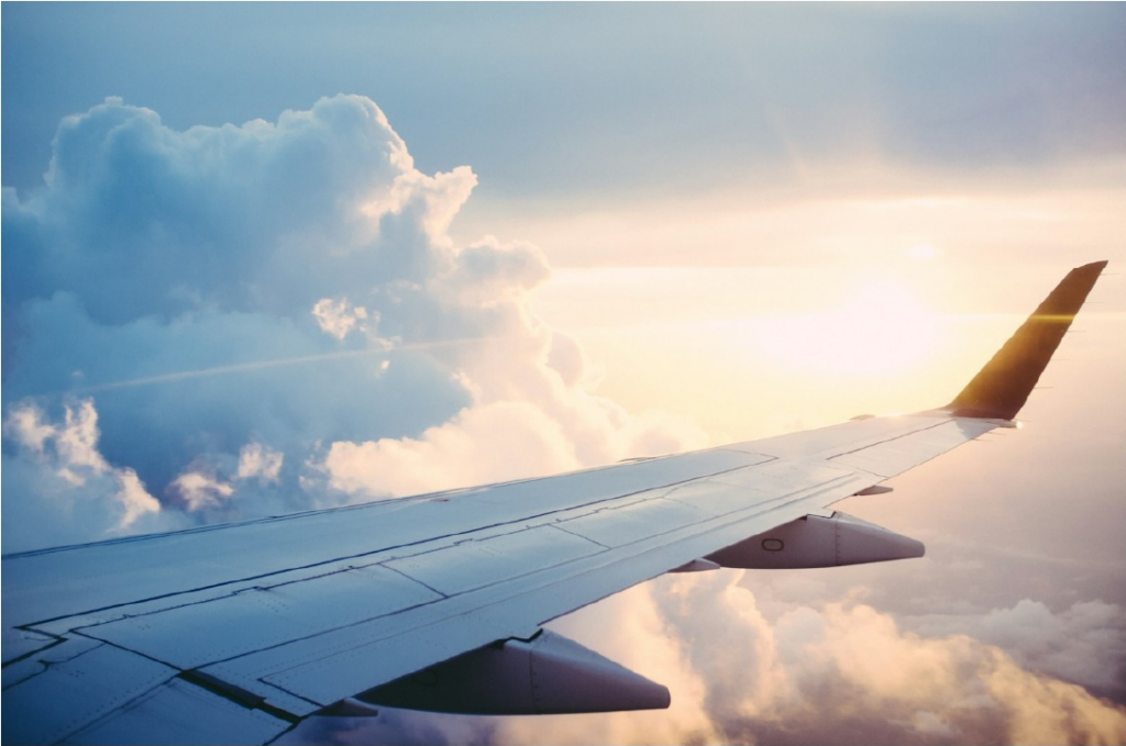 飛行中の飛行機の主翼の奥に雲と夕日が見える