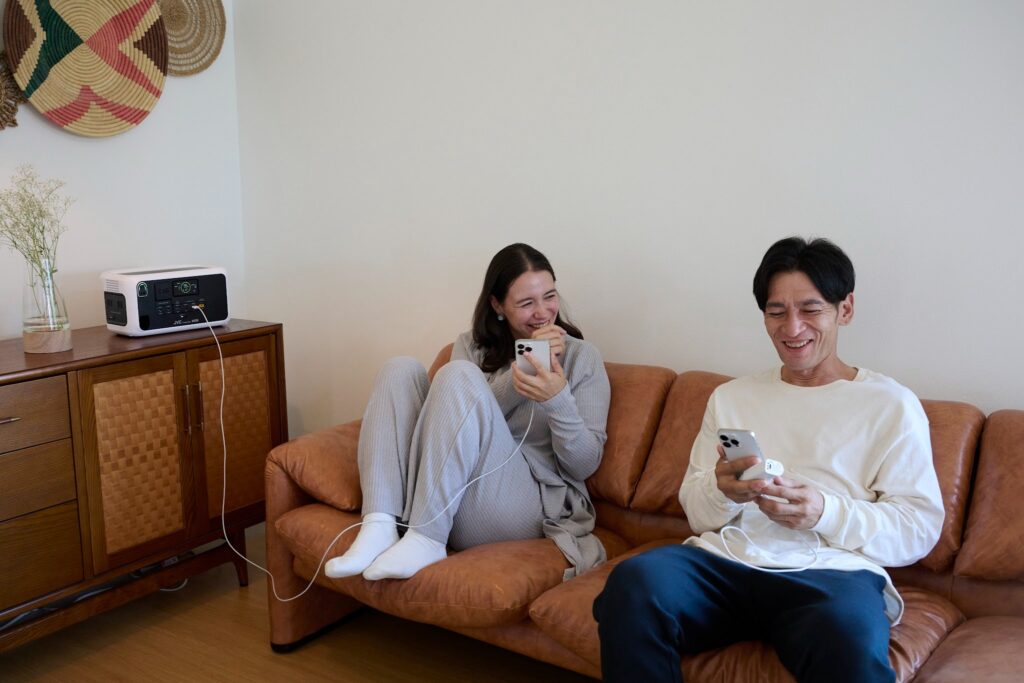 リビングのソファでポータブル電源からスマホを充電しながら笑顔でくつろぐ男女