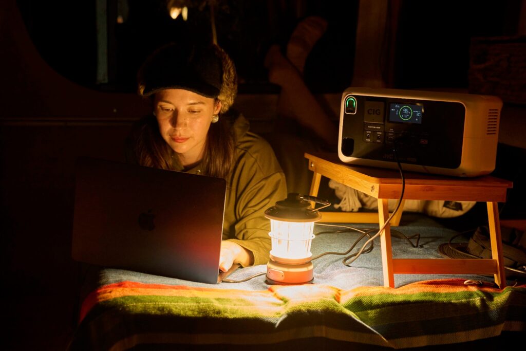 車中泊でランタンの灯りの下ポータブル電源からMacBookに給電しながら作業する女性